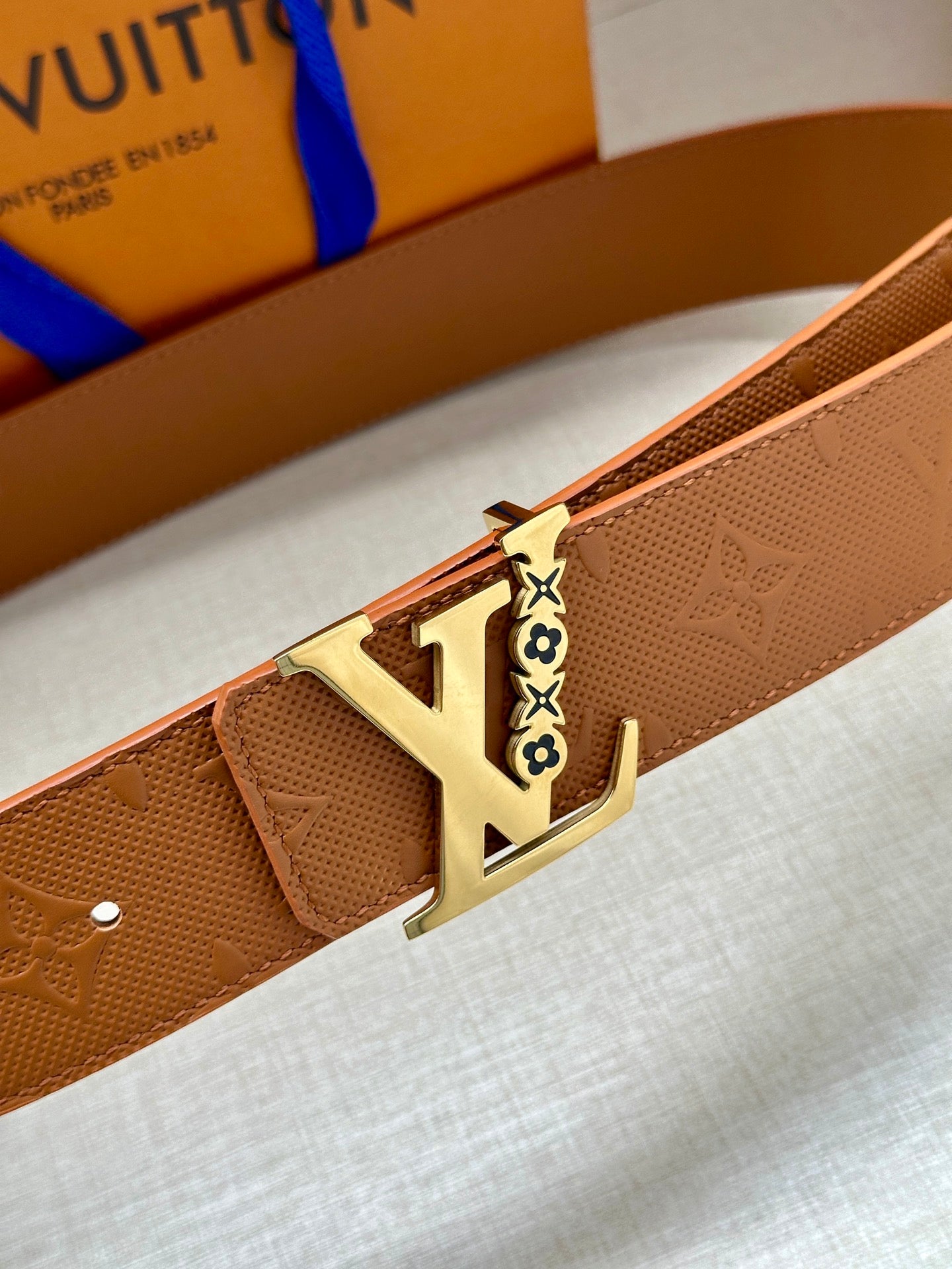 Louis Vuitton belt buckle close-up on tan leather strap with embossed texture
