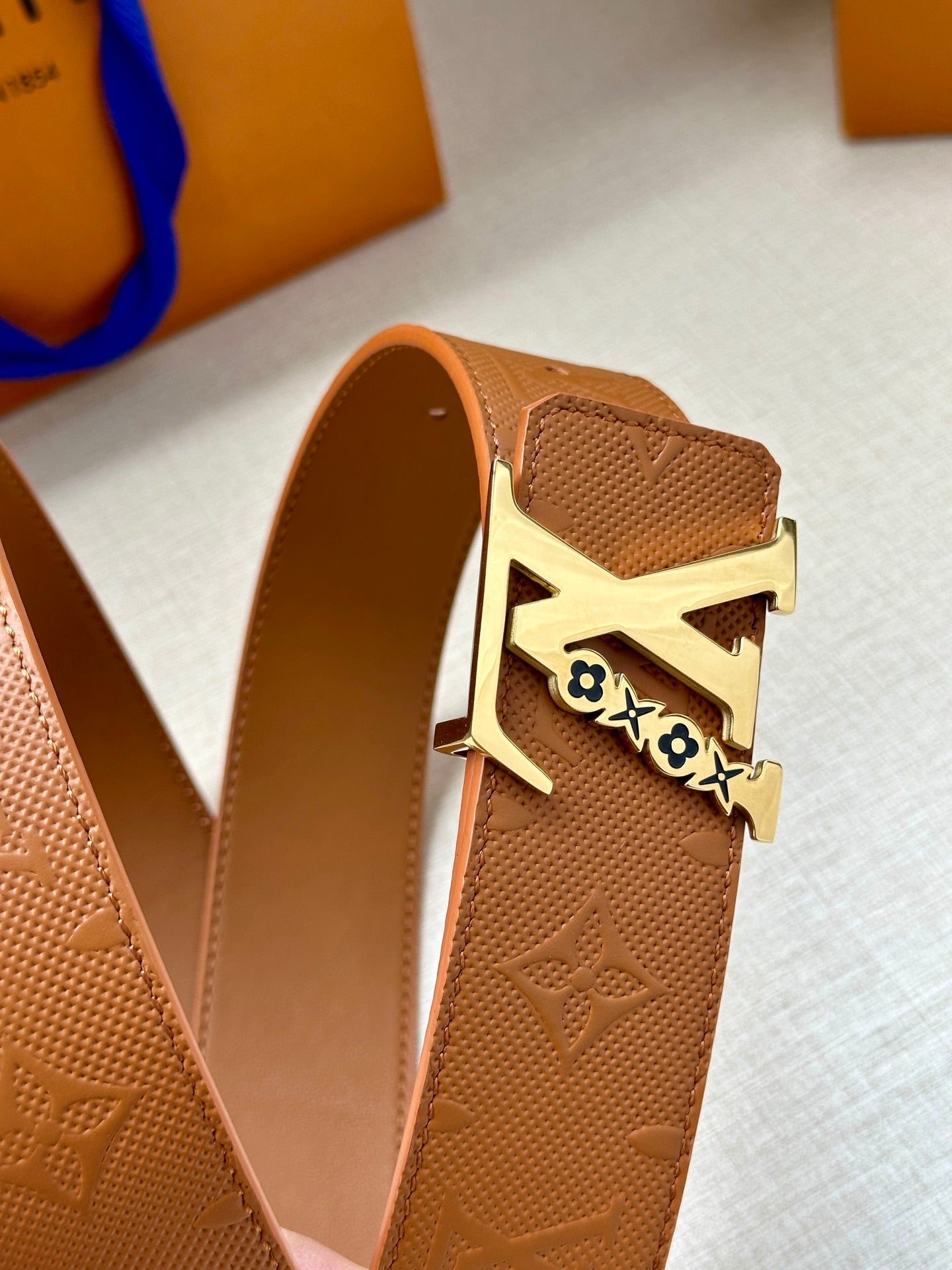 Louis Vuitton belt with tan leather strap and gold buckle with LV logo, side view