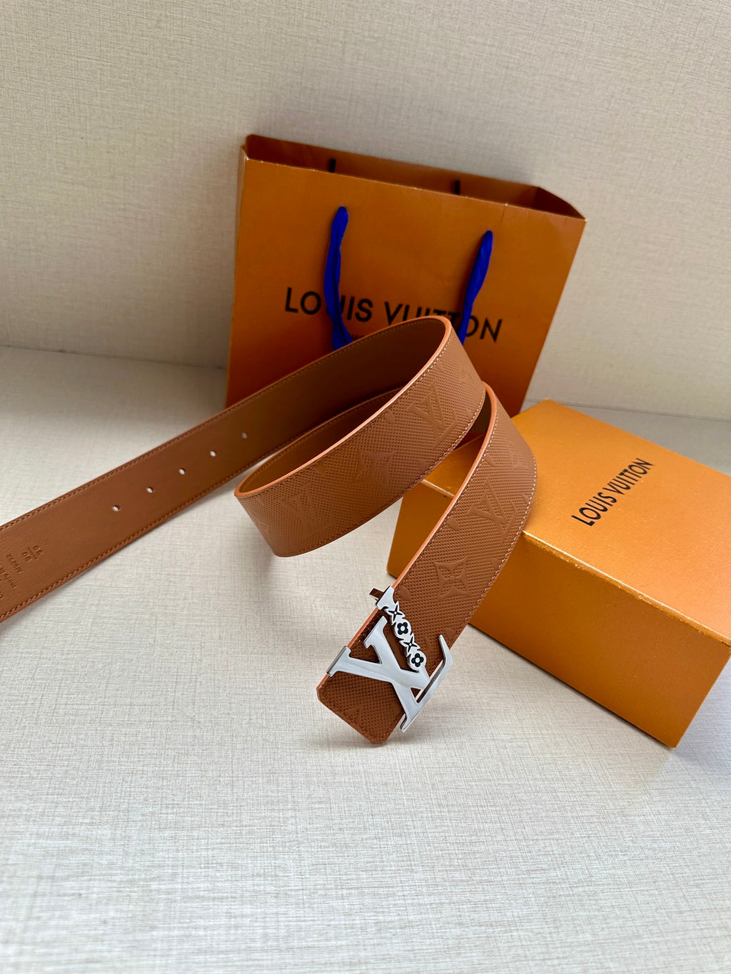 Louis Vuitton belt buckle on tan leather strap with embossed pattern and gold LV emblem