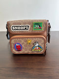 Coah bag crossbody with Snoopy patches on brown patterned exterior and flap