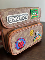 Coah bag close-up: Snoopy logo patch and character patches on brown exterior