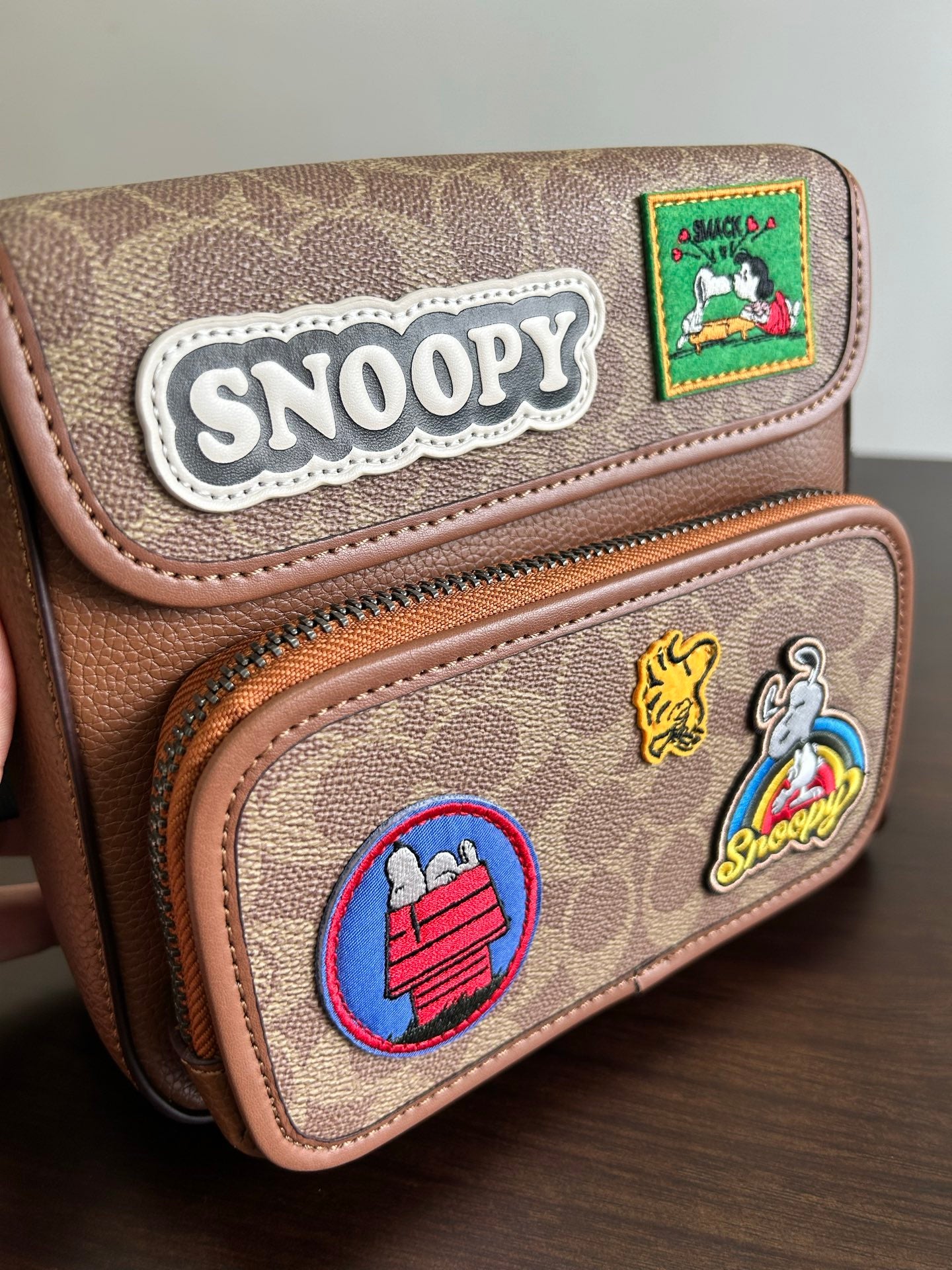 Coah bag close-up: Snoopy logo patch and character patches on brown exterior