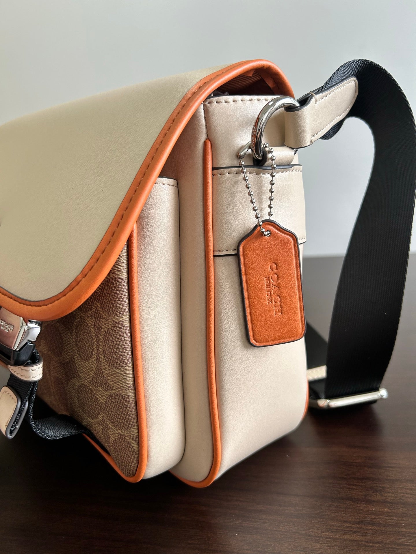 Beige crossbody bag side view with orange trim, key ring charm, and strap