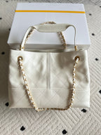 White quilted Chanel tote bag style with gold chain straps and CC front