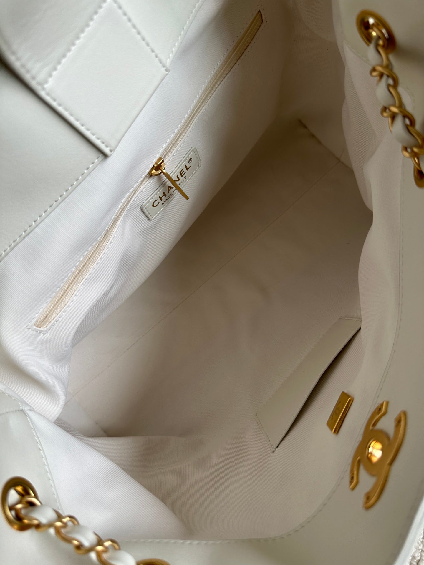 Open white Chanel bag interior with gold zipper pull and stitching