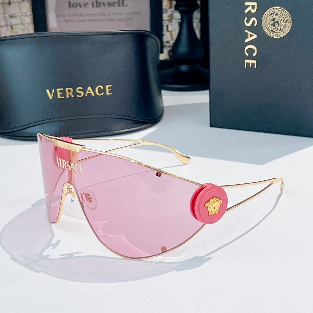 Sunglasses with gold-tone frame and pink lenses, round red logo medallion on temple.