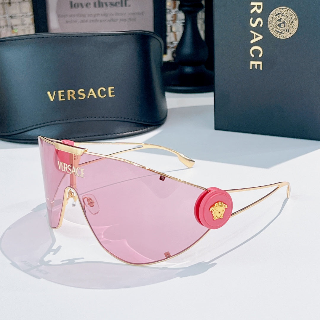 Sunglasses with gold-tone frame and pink lenses, round red logo medallion on temple.