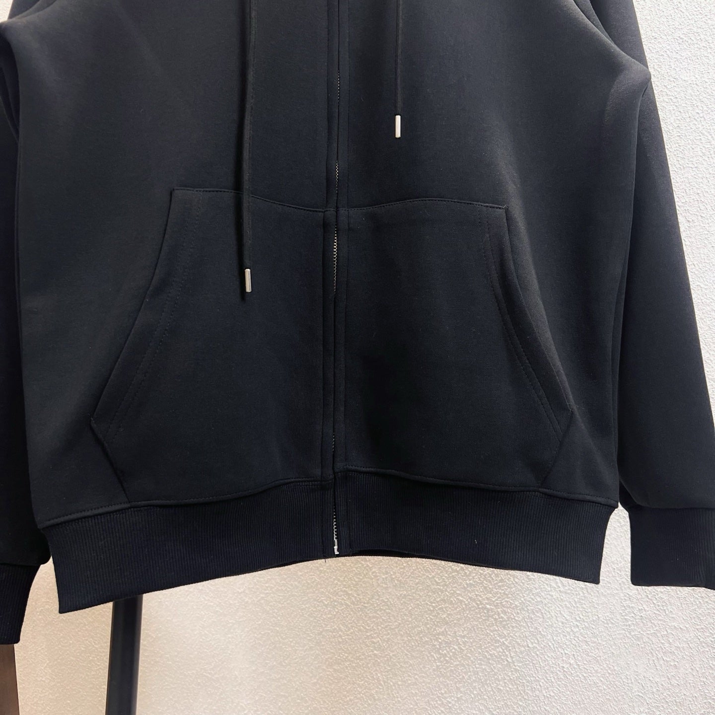 Dark zip-up hoodie with kangaroo pocket and ribbed hem, visible metal zipper pulls