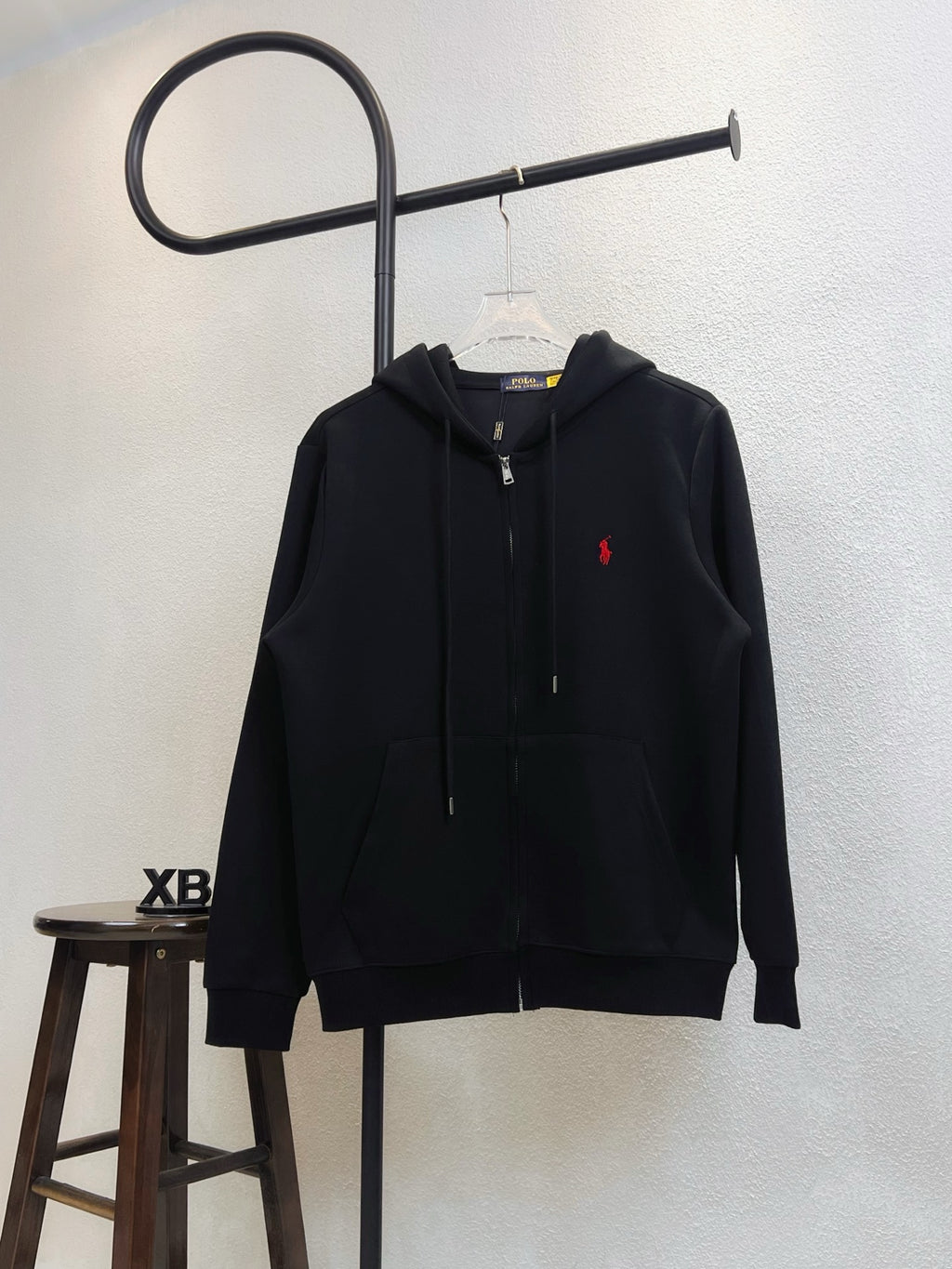 Black zip-up hoodie with adjustable hood and red polo logo