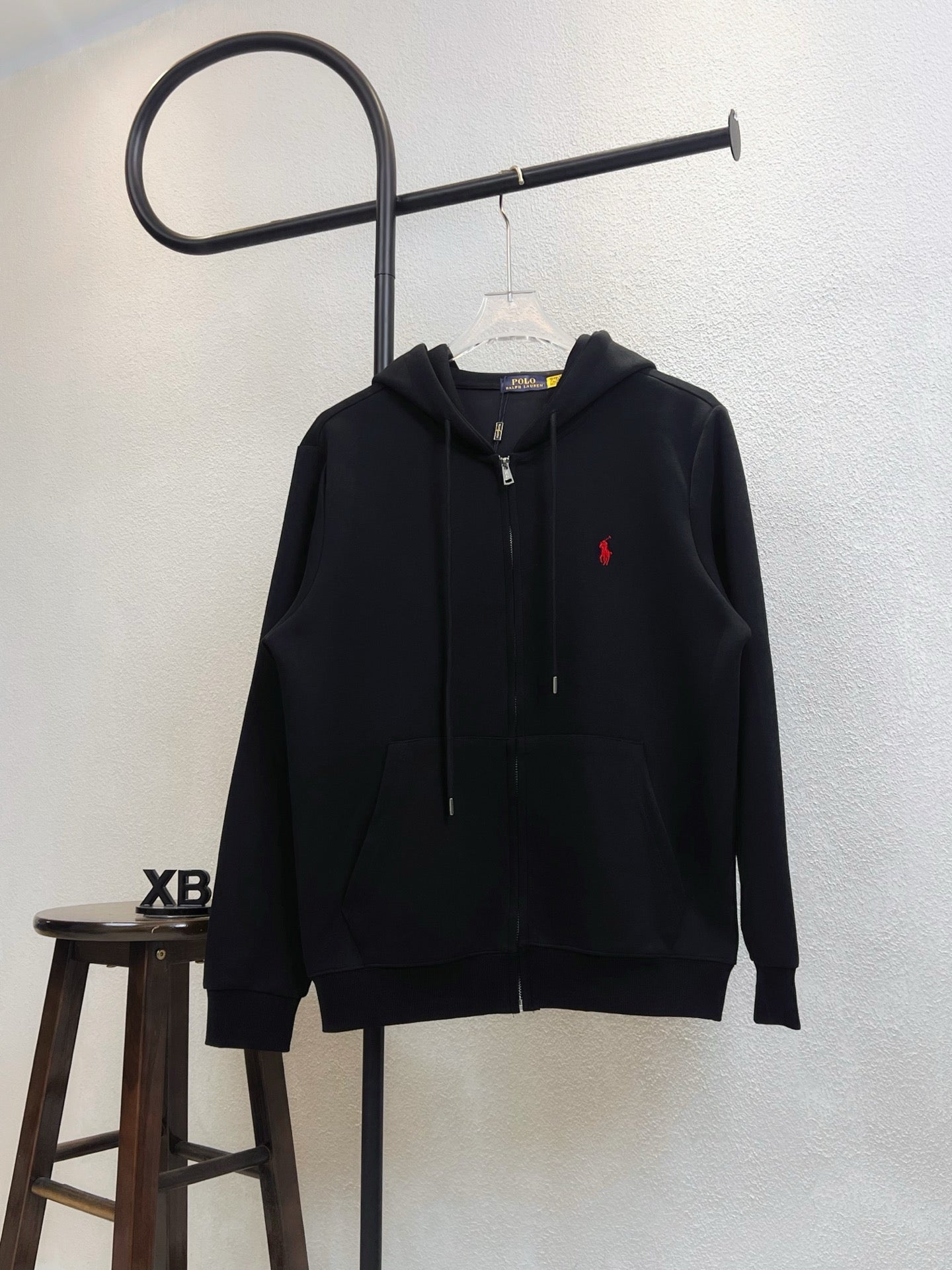 Black zip-up hoodie with adjustable hood and red polo logo