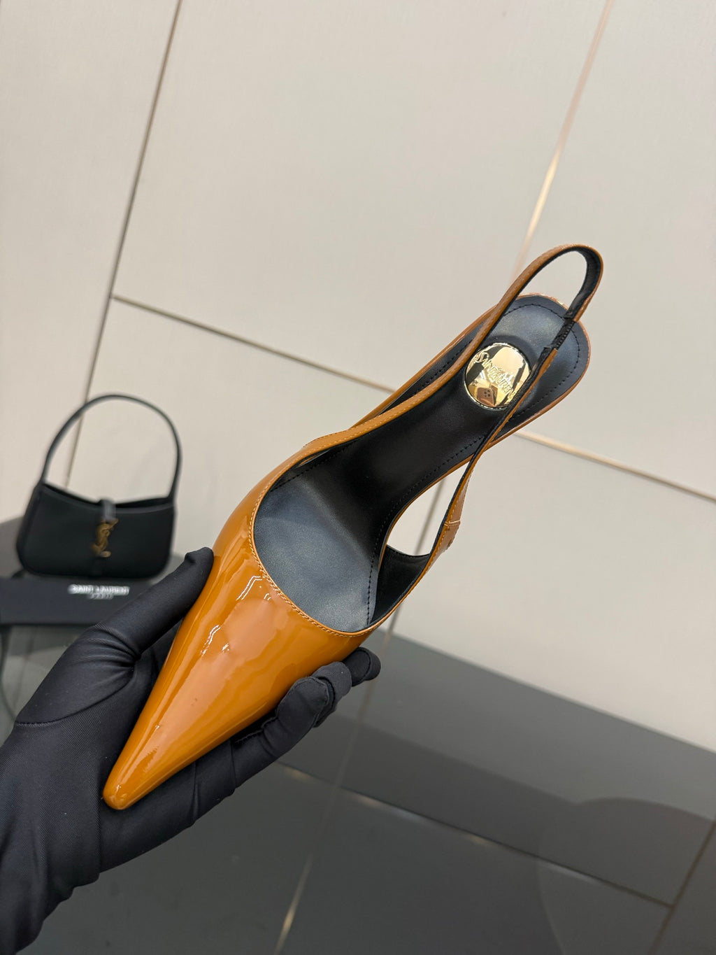 Women's orange pointed-toe slingback pump held in a gloved hand; black heel counter.