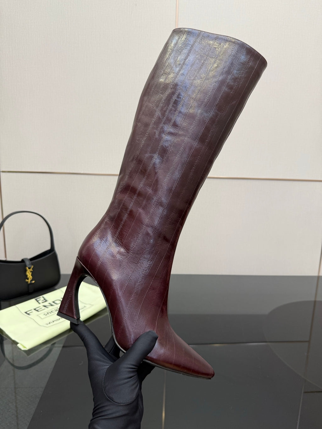 Knee-high boot held up, dark burgundy leather with pointed toe and slim heel