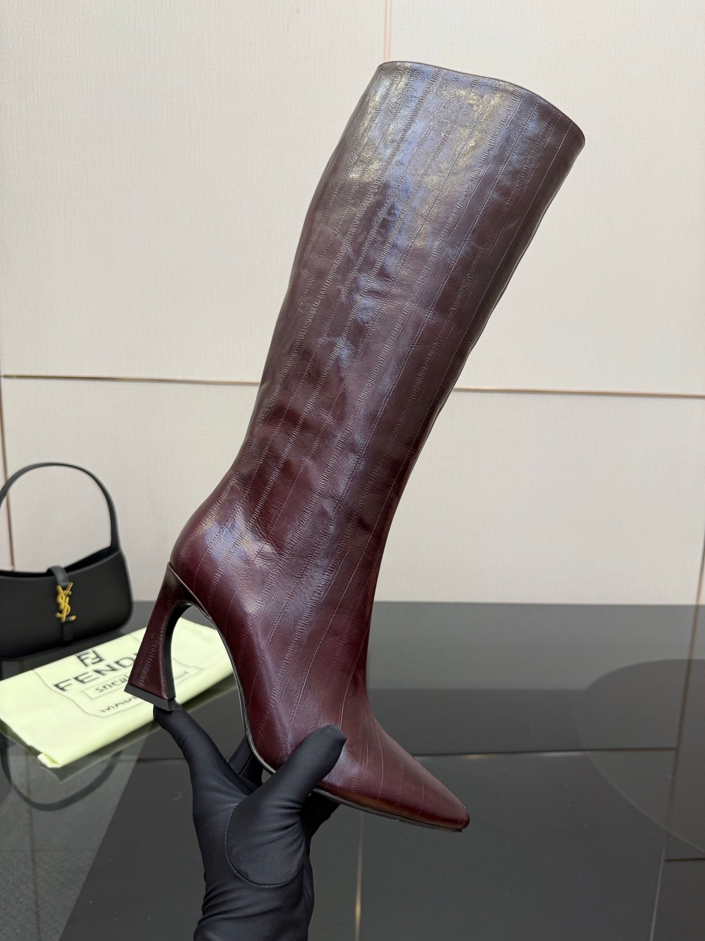 Knee-high boot held up, dark burgundy leather with pointed toe and slim heel