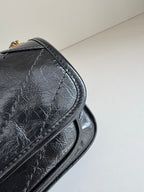YSL dark leather bag close-up of arched side, stitched edge and curved flap