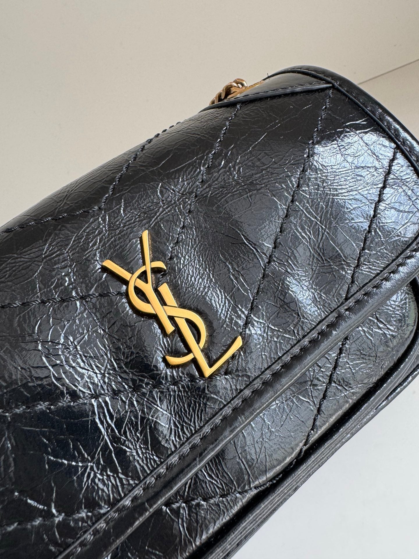 YSL dark leather flap bag with gold YSL emblem and decorative stitching