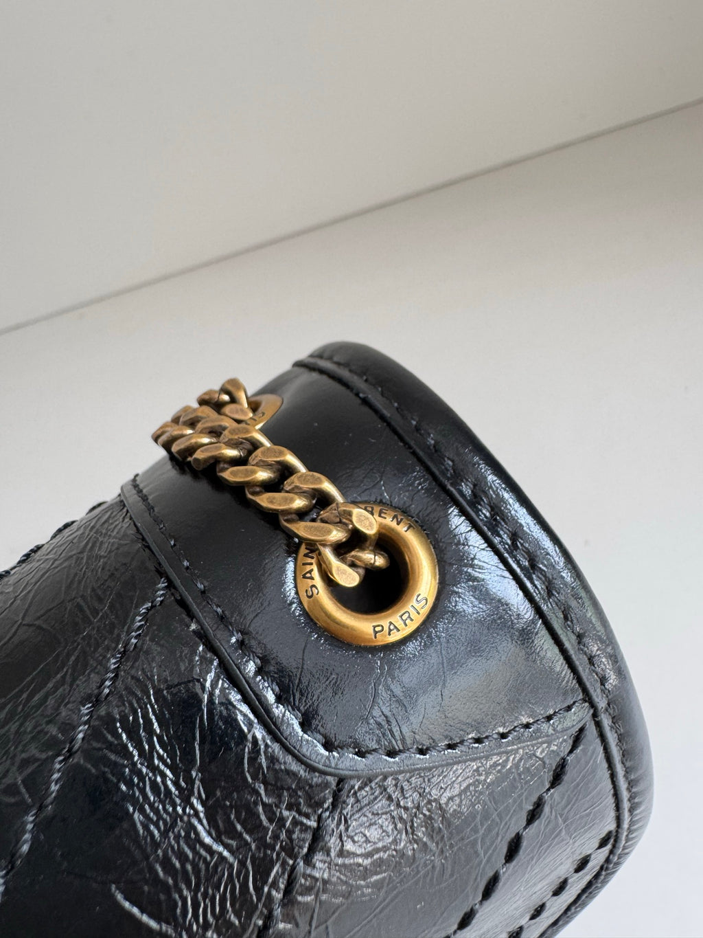 YSL dark leather bag detail with gold ring clasp, stitched flap and textured finish