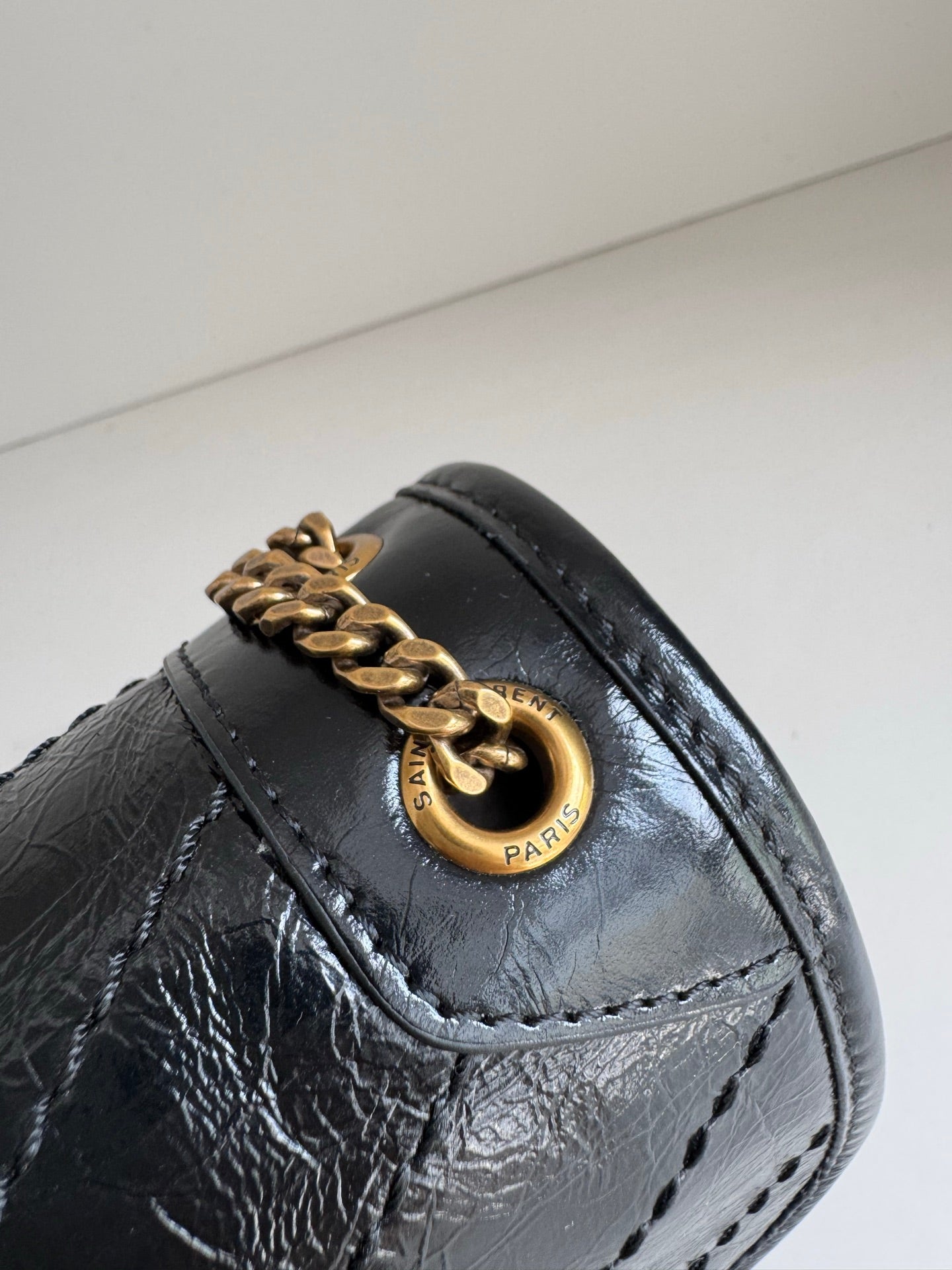 YSL dark leather bag detail with gold ring clasp, stitched flap and textured finish