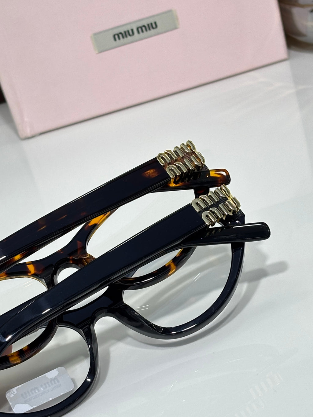 MiuMiu glasses side view with navy frame, tortoiseshell tips, and gold logo hardware