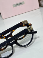 MiuMiu glasses side view with navy frame, tortoiseshell tips, and gold logo hardware