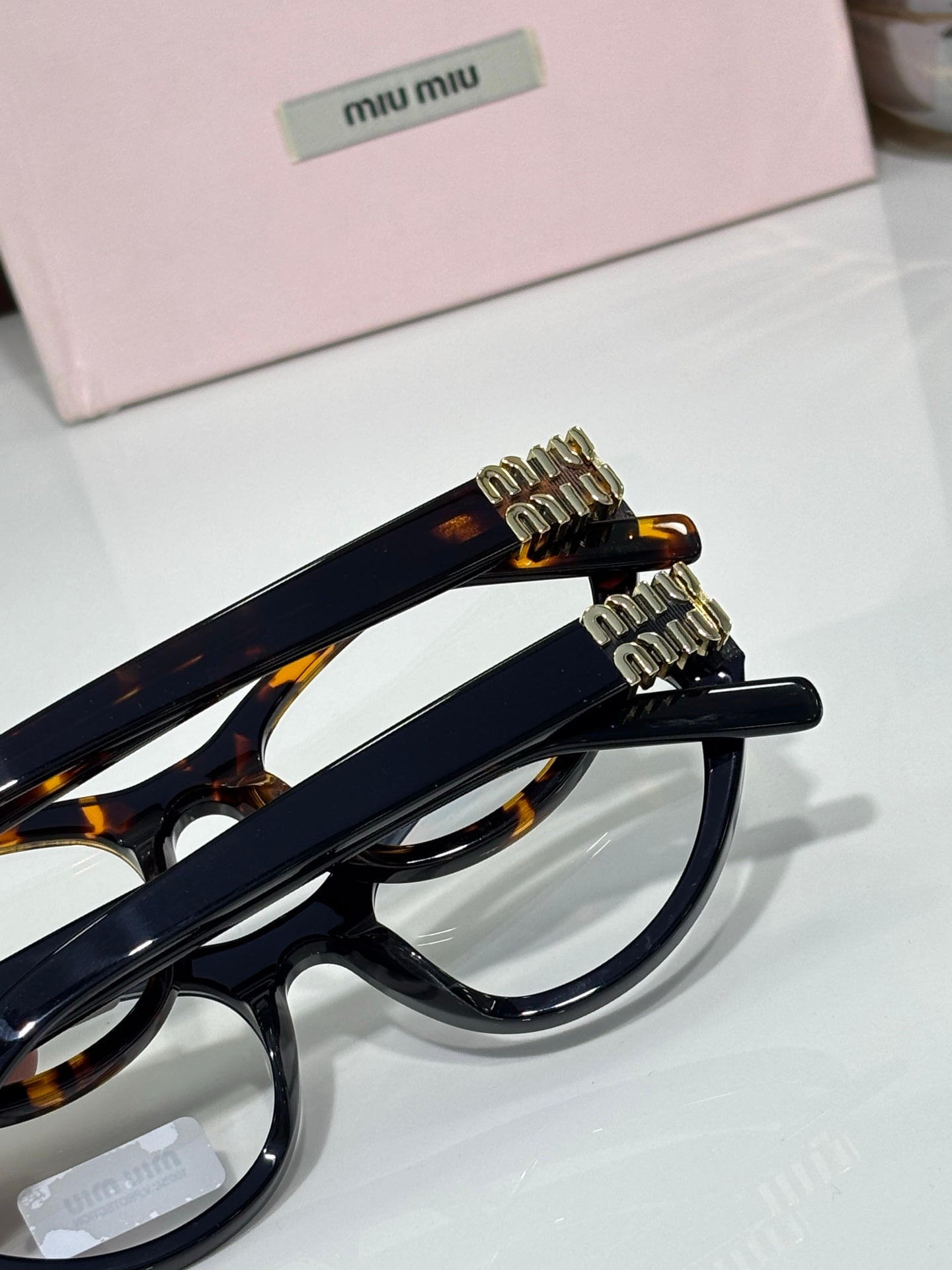 MiuMiu glasses side view with navy frame, tortoiseshell tips, and gold logo hardware