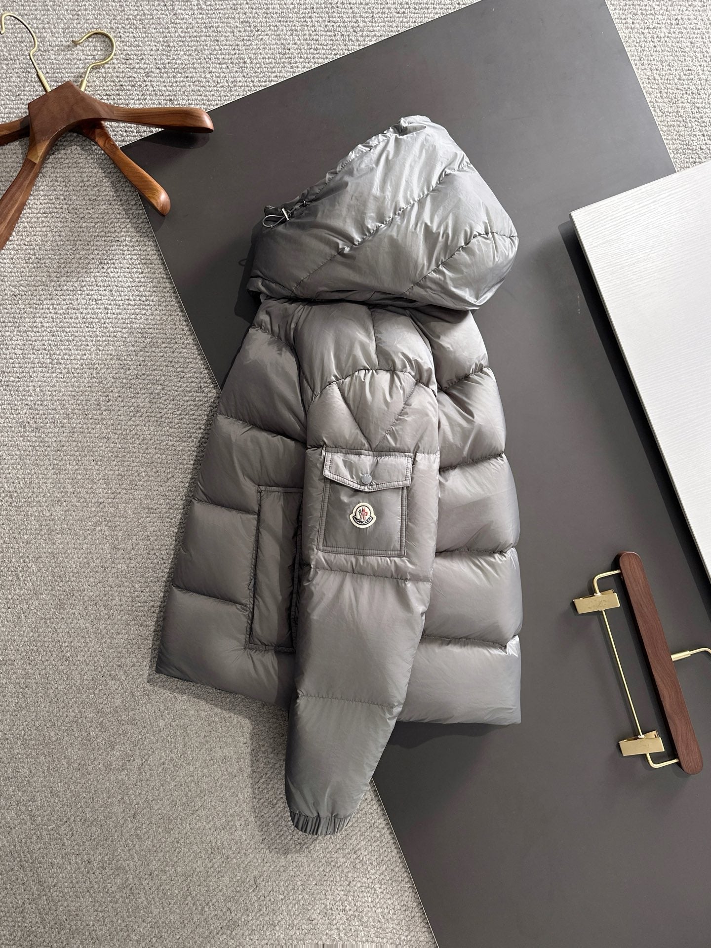 Gray long puffer jacket with attached hood, front zipper, and patch pocket on sleeve