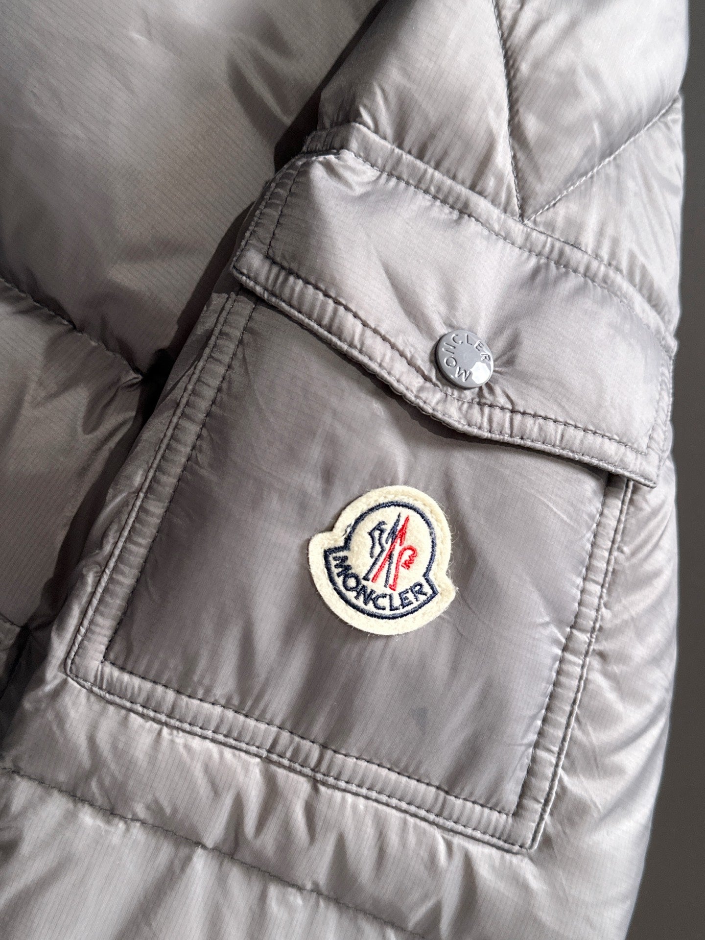 Gray puffer jacket sleeve with round logo patch near cuff