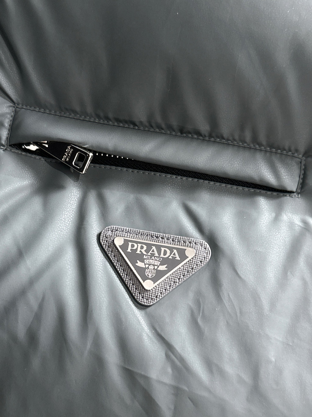 Prada triangular logo patch on dark gray quilted puffer vest fabric
