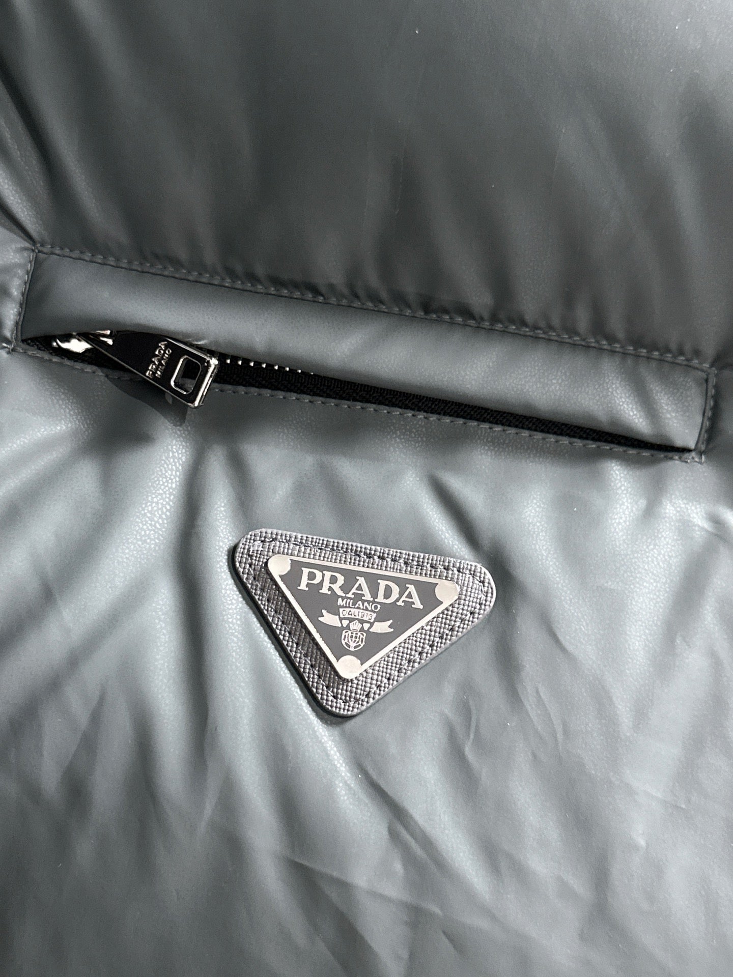 Prada triangular logo patch on dark gray quilted puffer vest fabric