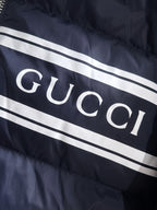 Gucci puffer jacket chest stripe with large “GUCCI” lettering on navy fabric