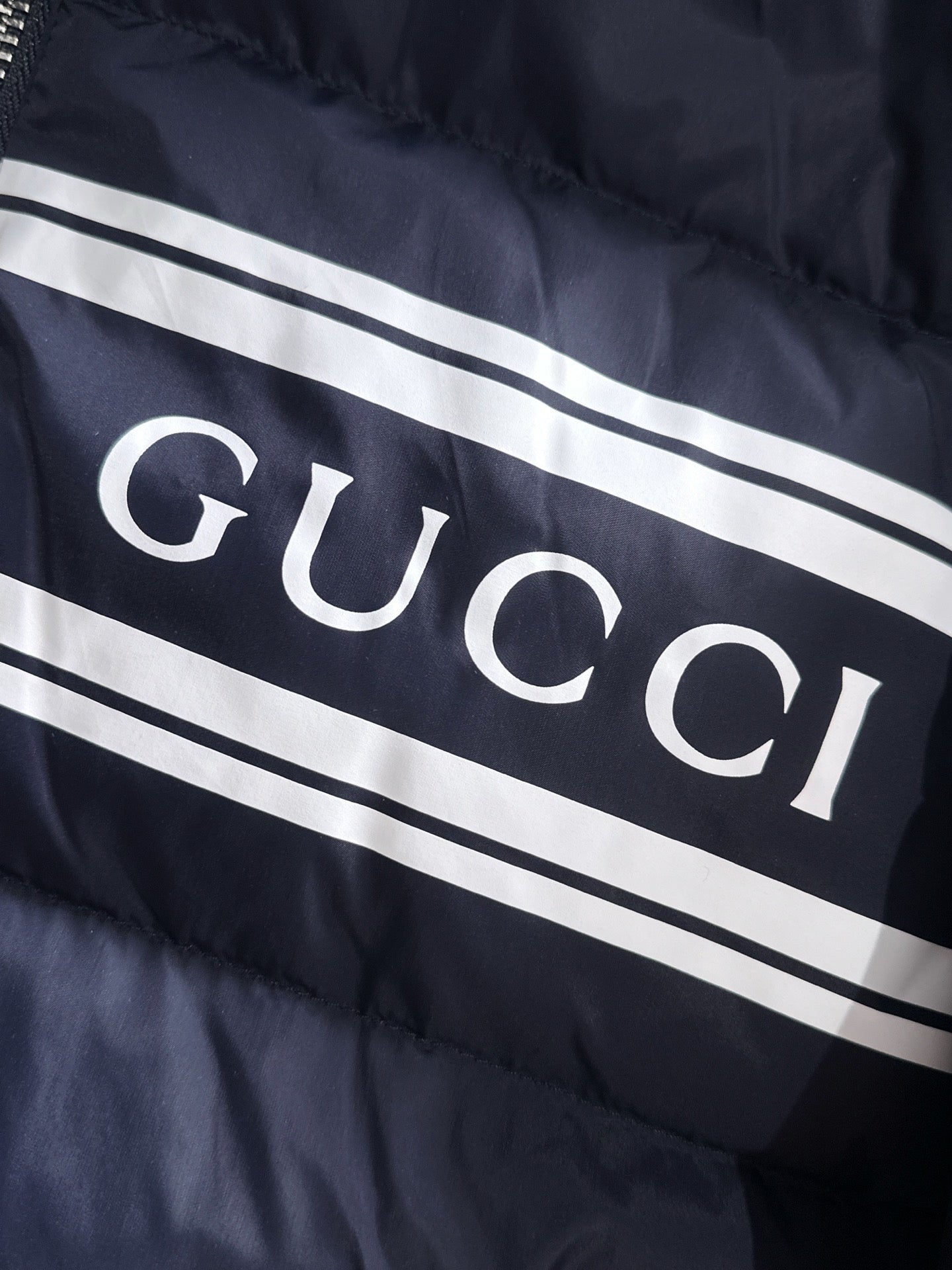 Gucci puffer jacket chest stripe with large “GUCCI” lettering on navy fabric