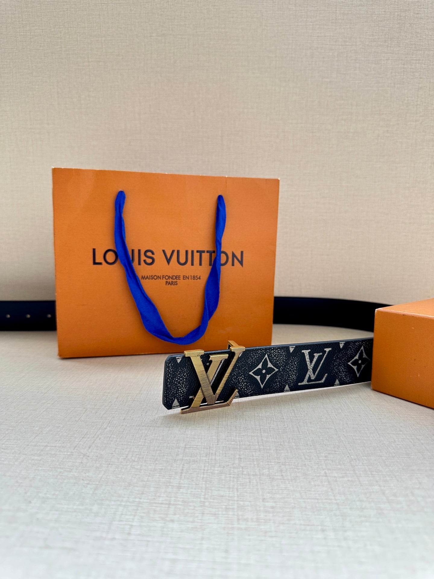 Monogram belt with gold-tone buckle and dark patterned strap, laid flat