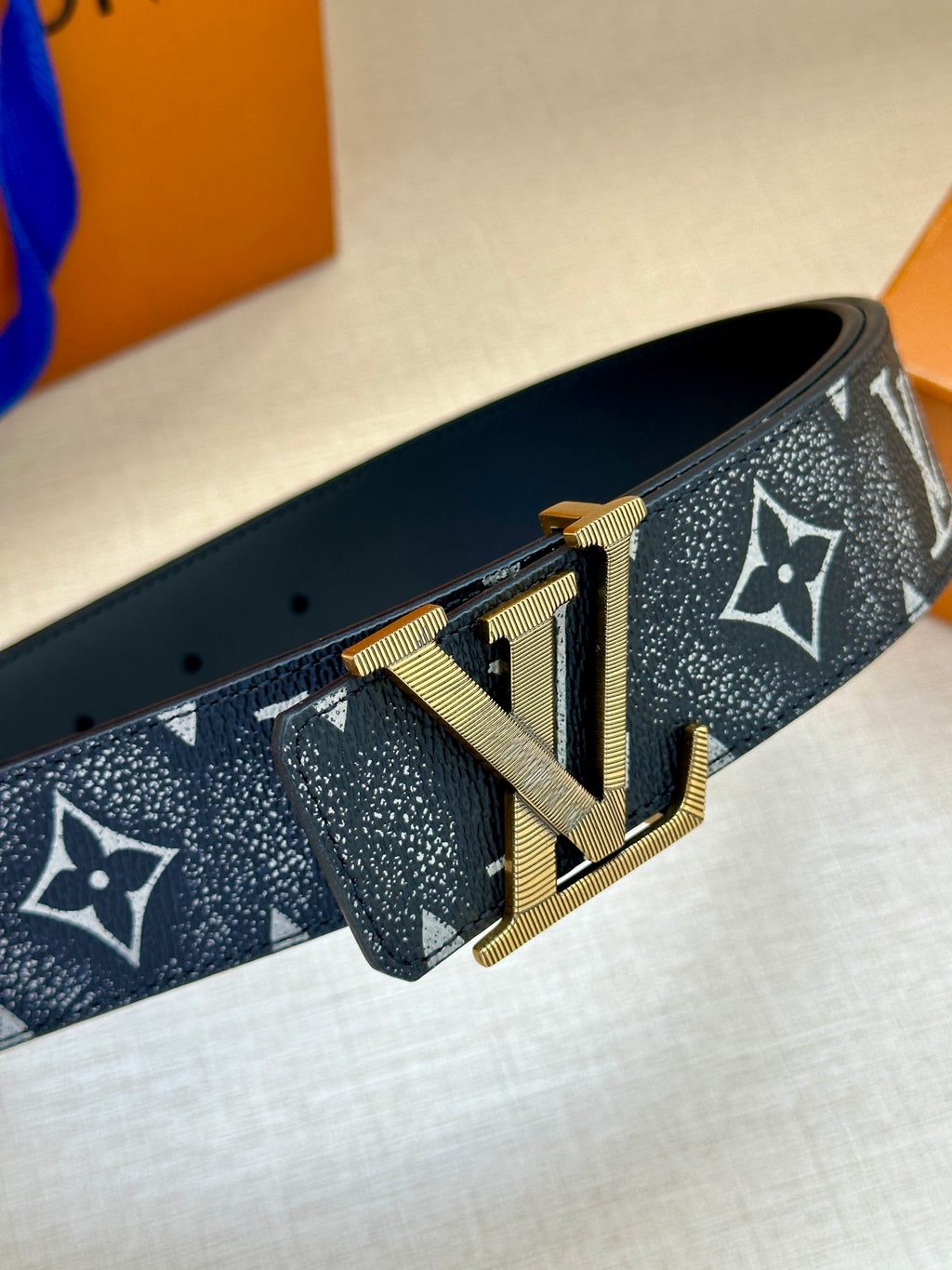 Monogram belt side view with gold-tone buckle on dark patterned strap