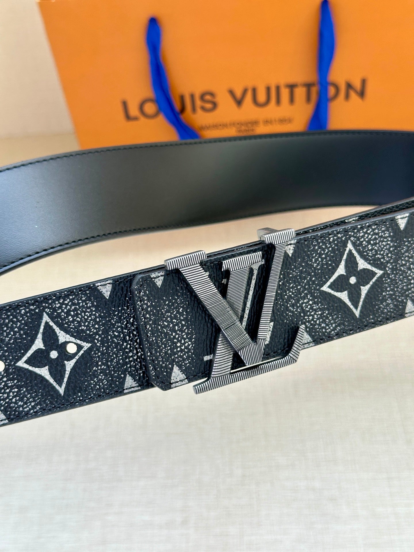 Monogram belt close-up with gold-tone buckle and dark patterned strap