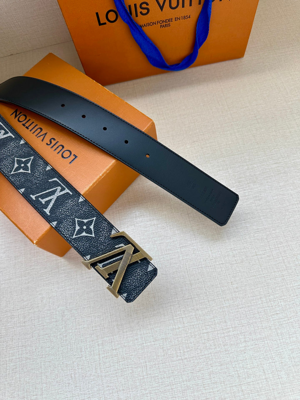 Monogram belt detail with perforated dark strap and gold-tone buckle, flat