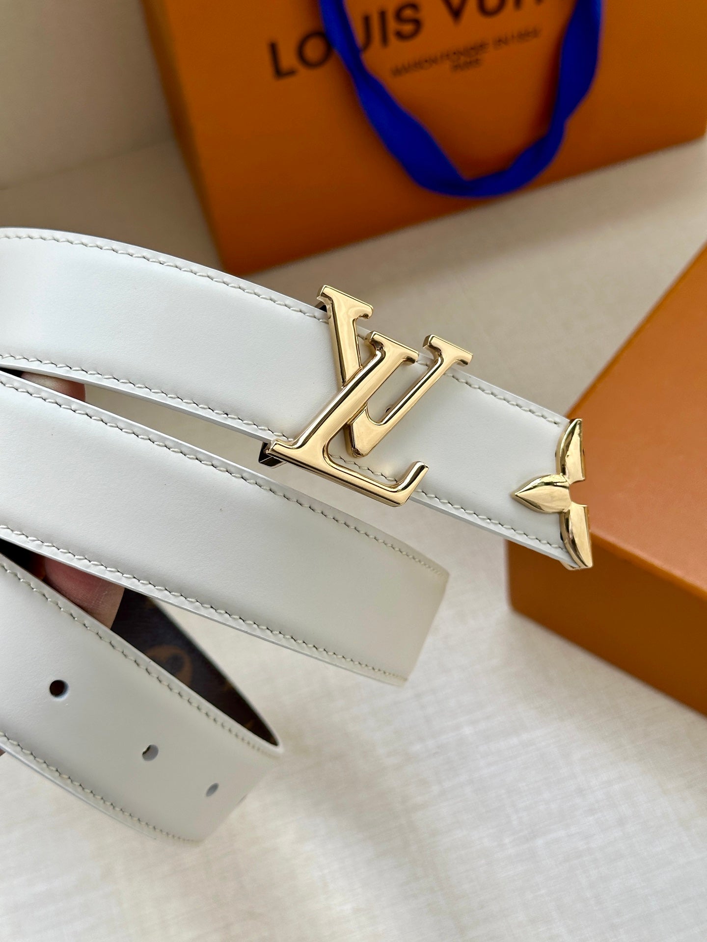 White leather belt with gold buckle and punched strap holes