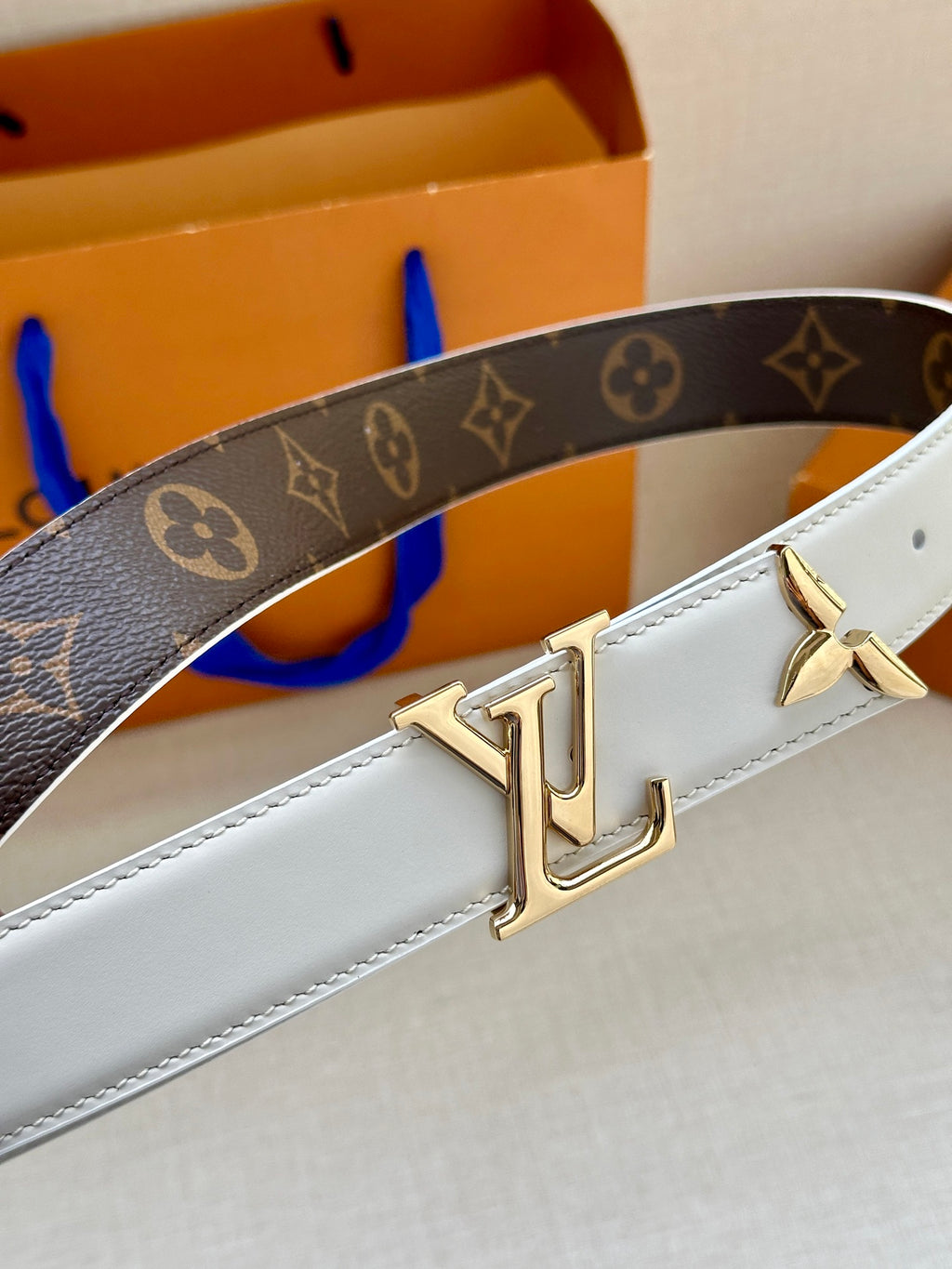 White leather belt with dark monogram strap and gold LV-style buckle hardware