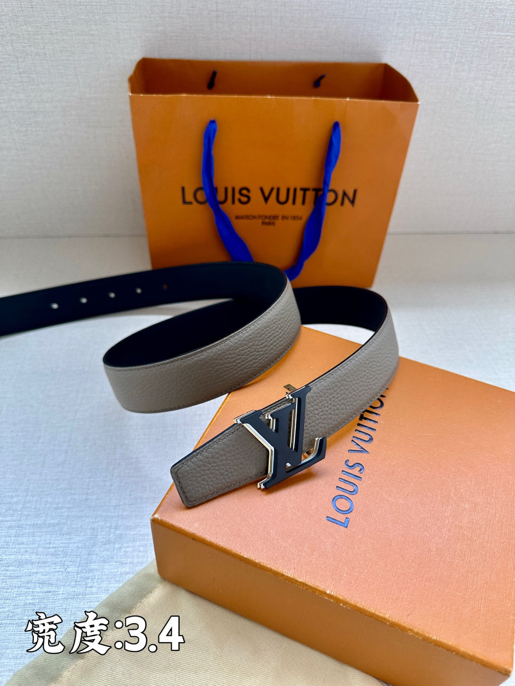 Grey leather belt with gold-tone LV buckle, shown on the box