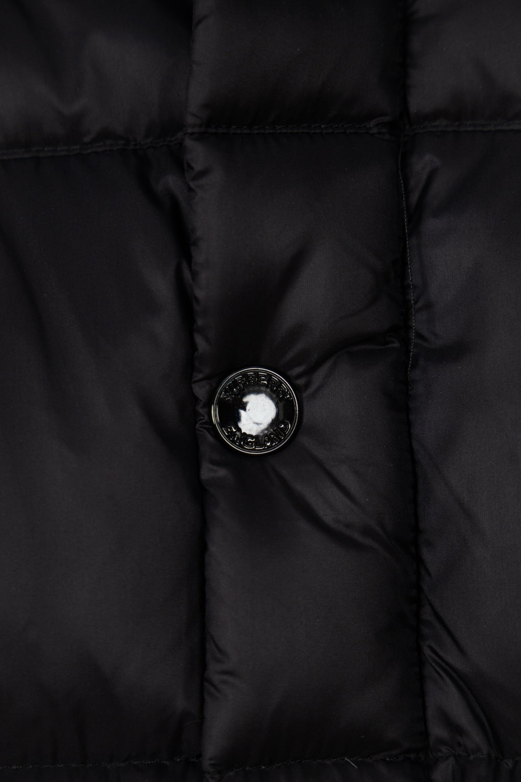 Black puffer jacket front with round button and metal emblem center