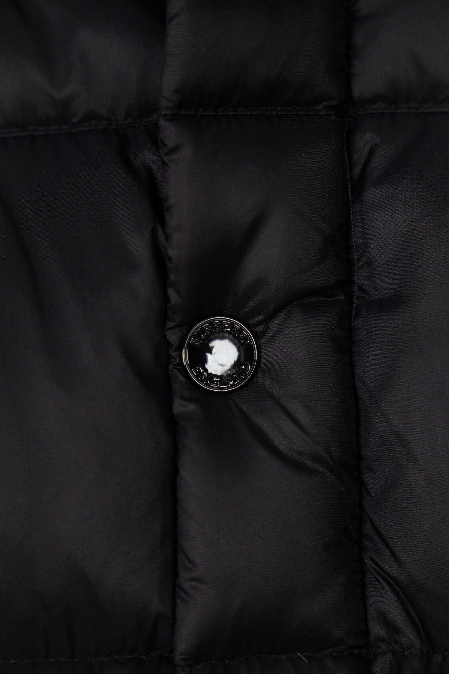 Black puffer jacket front with round button and metal emblem center