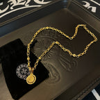 Gold link necklace with round pendant on a black display card atop tray
