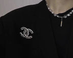 Rhinestone Chanel logo brooch on black blazer, silver-tone stones