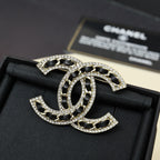 Rhinestone logo brooch with black enamel center, gold-tone border