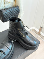 Dark quilted high-top boots with lace ties, gold hardware, and chunky ribbed sole