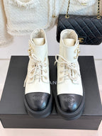 Pair of white lace-up ankle boots with black toe caps and gold logo detail, chunky sole