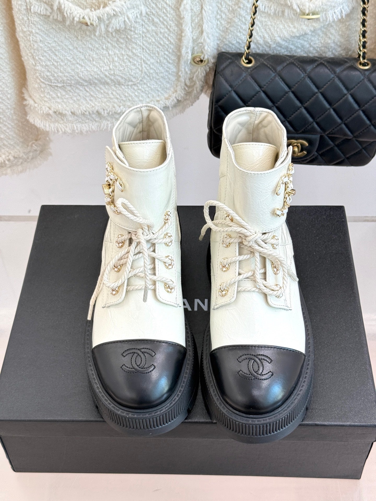 Pair of white lace-up ankle boots with black toe caps and gold logo detail, chunky sole