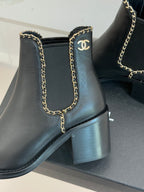 Close-up of ladies dark ankle boot with gold chain trim and Chanel-style emblem