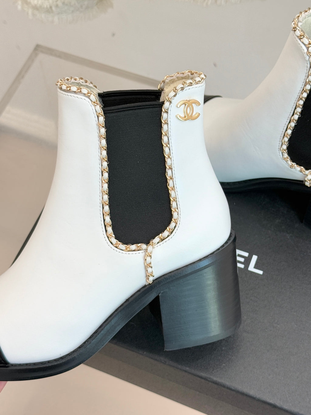 White ankle Chelsea boot with gold trim on elastic side and block heel.