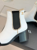 White ankle Chelsea boot with gold trim on elastic side and block heel.