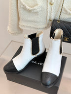 White and black Chelsea boots with gold trim and elastic side panels on box.