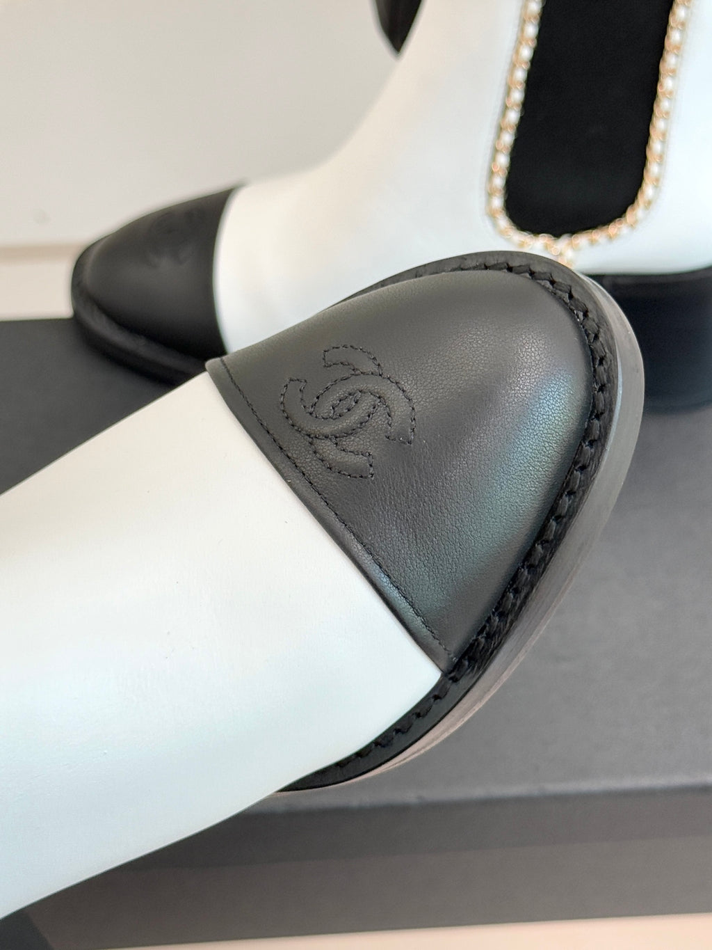 White and black Chelsea boot detail showing black toe cap and embossed logo.
